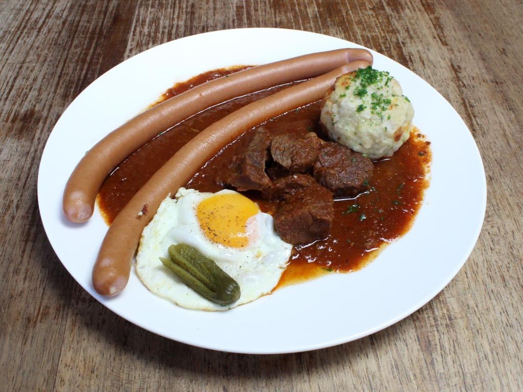 Fiakergulasch mit Semmelknödel, Sacherwürstel, Spiegelei und Fächergurkerl